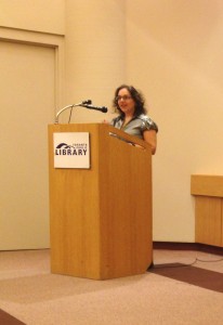 A photo of author A.M. Matte at a Toronto Public Library podium, reading a short story excerpt .
