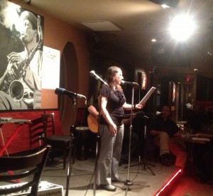 Under a spotlight and by a few microphones, A.M. Matte reads excerpts of her short story, Paper Dolls