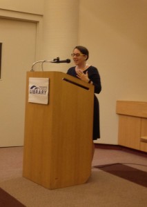 A.M. Matte reading an excerpt of Paper Dolls at the Toronto Public Library Main Reference Branch, at a wooden podium.